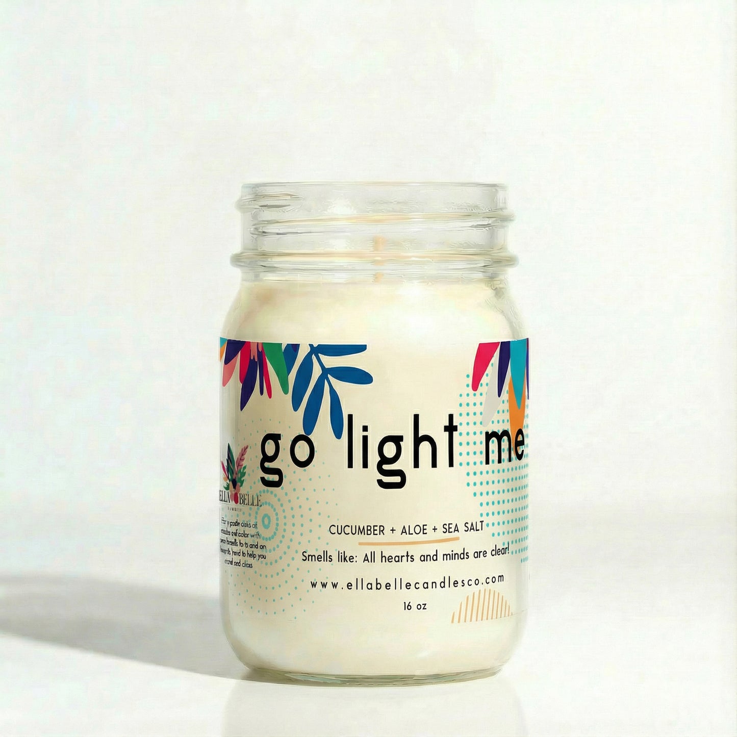 Candle in a glass jar labeled " Go Light Me" with a decorative label on a white background