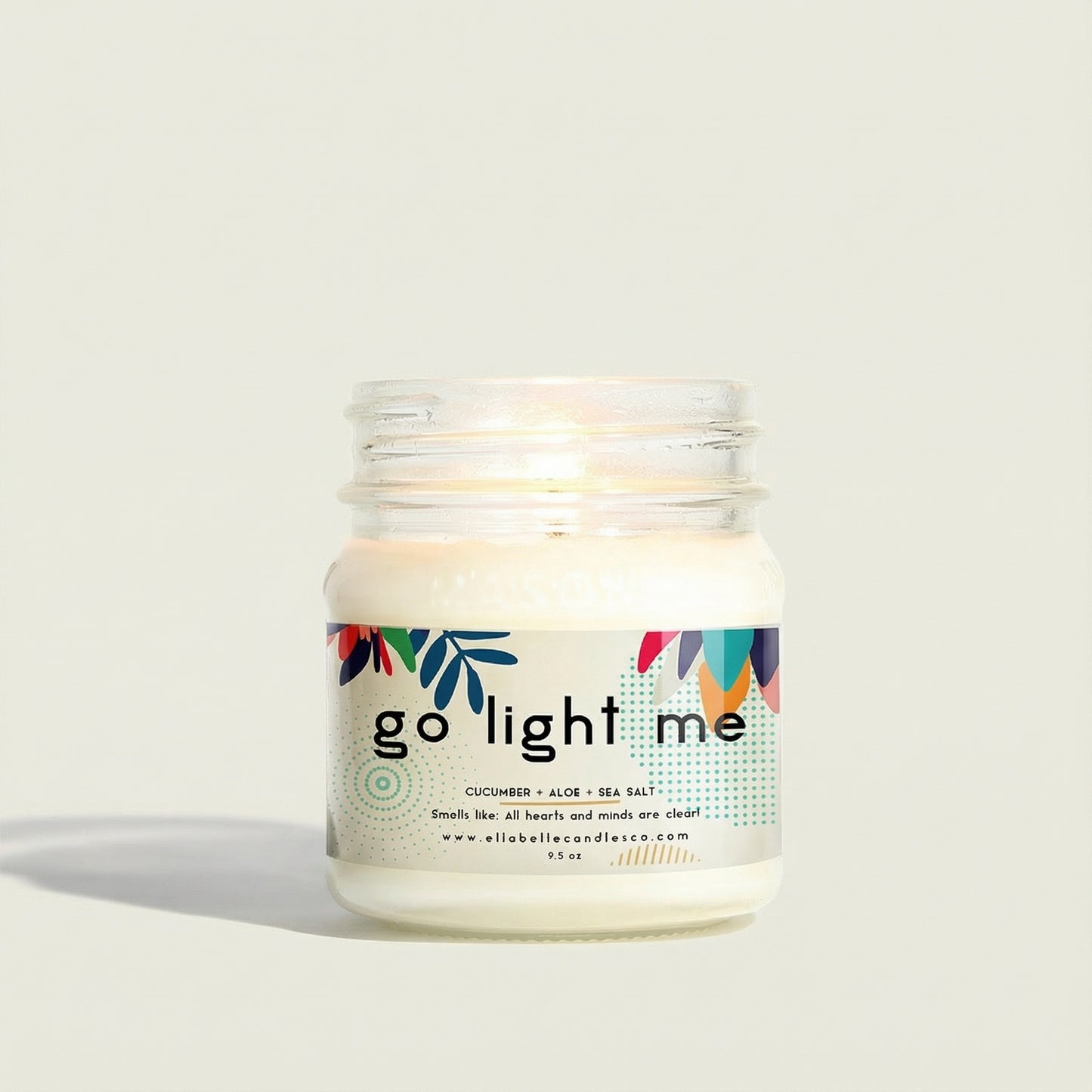 Candle in a glass jar labeled " Go Light Me" with a decorative label on a white background