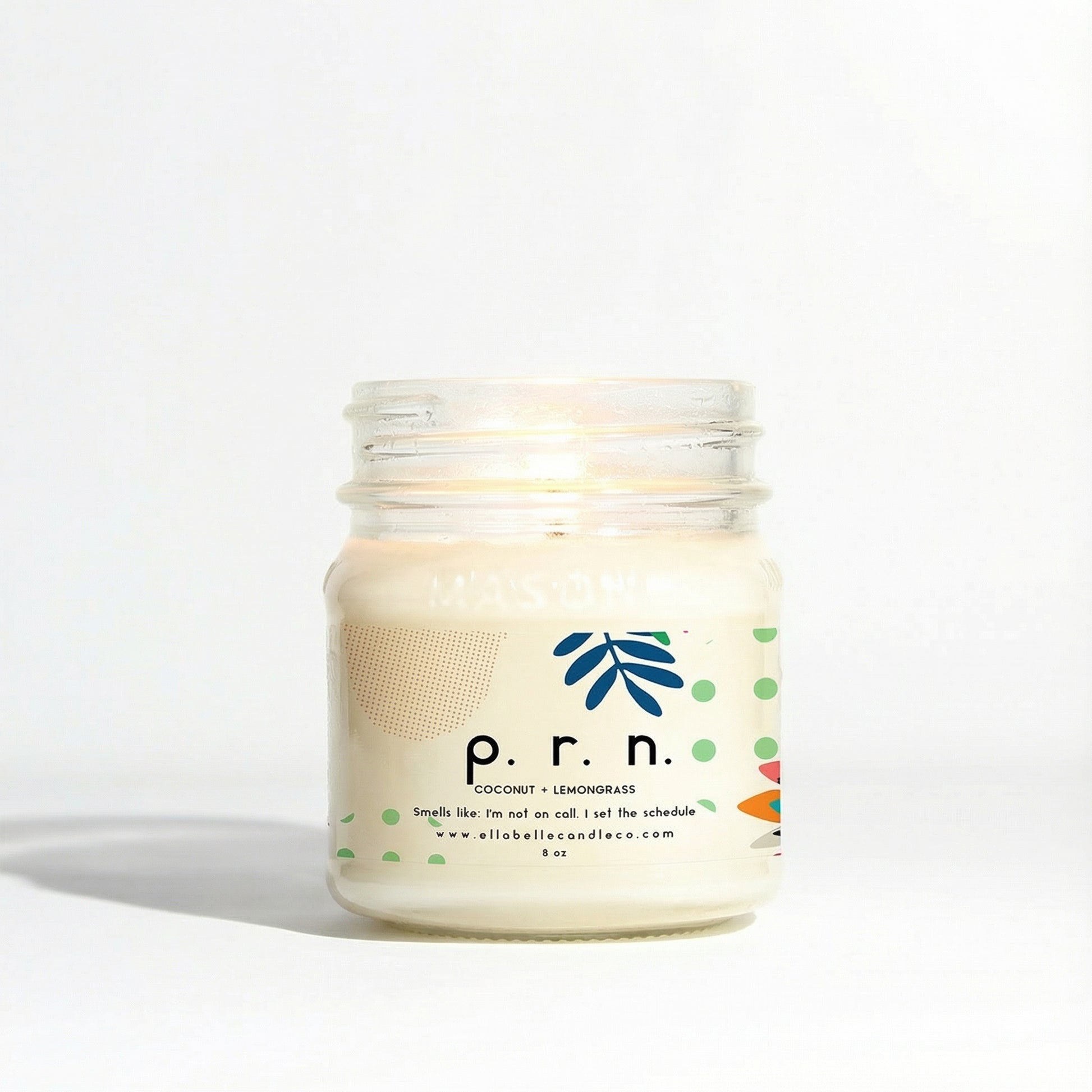 A mason jar candle with a label that reads 'P.R.N.', coconut + lemongrass with a white wax cap and a lit wick.