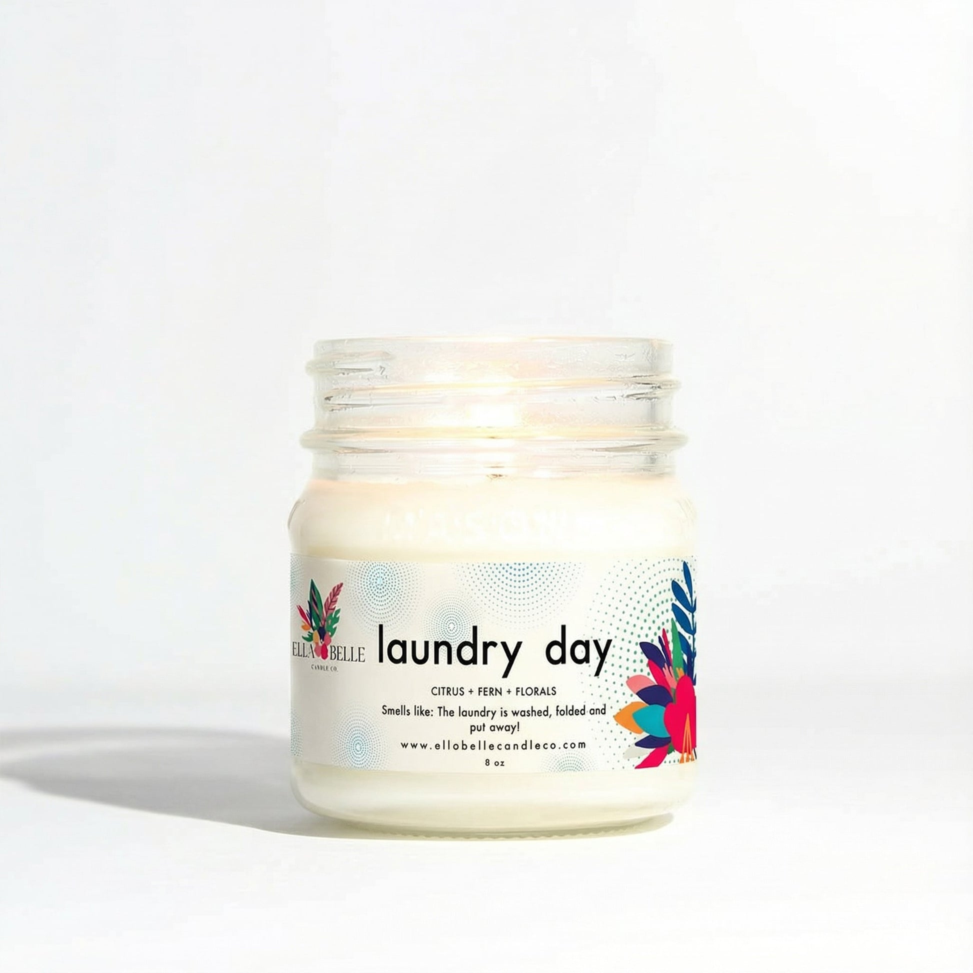 Jar of candle labeled 'laundry day' with colorful design on a white background